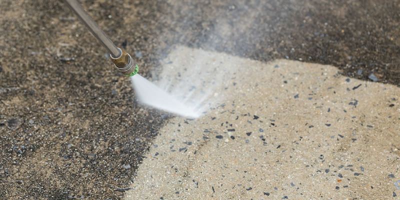 Pressure washer cleaning a dirty concrete surface, revealing a clean area.