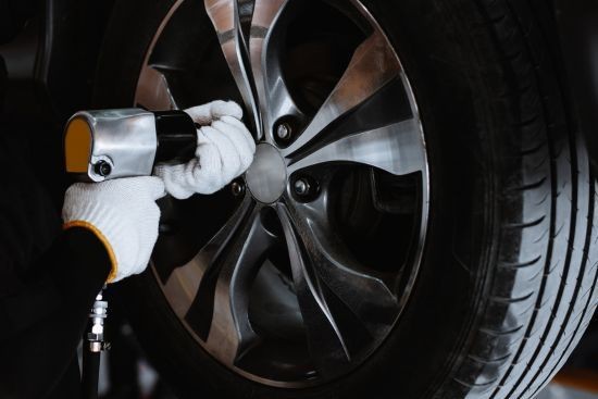 Mechanic using a tool to tighten bolts on a car wheel, wearing white gloves for protection.