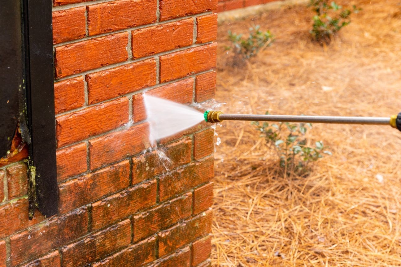 Close-up of a high-pressure water jet cleaning a brick wall outside, removing dirt and grime.